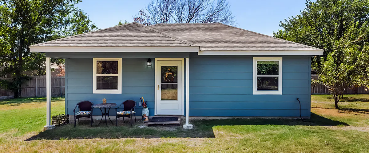 Blue home addition with a covered front porch and newly installed siding, set in a lush green backyard.