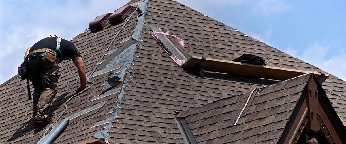 Contractor installing asphalt shingles on a steep residential roof for a roof repair project.