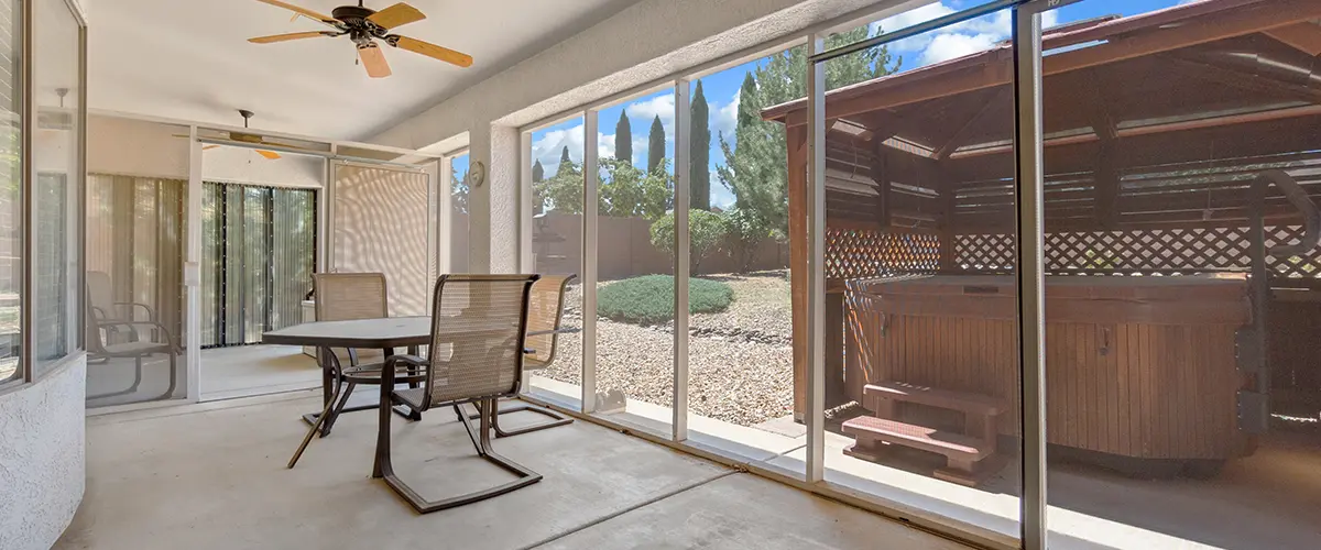 Enclosed patio with a ceiling fan and sliding doors, offering a relaxing outdoor space with a view of a hot tub and landscaped yard.