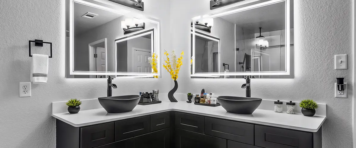 Modern bathroom with black vanity, illuminated mirrors, and stylish vessel sinks, creating a sleek and contemporary design.