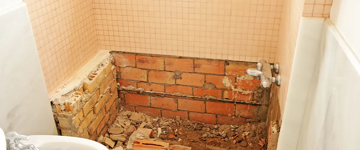 Old bathroom under renovation with demolished bathtub area exposing bricks and plumbing.