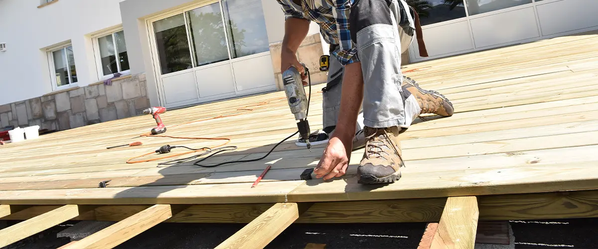 Professional contractor building a wooden deck, using a power drill for precise installation.