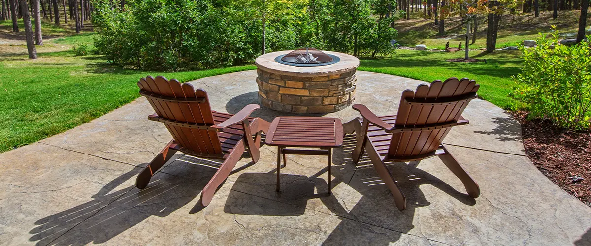 Relaxing backyard retreat with Adirondack chairs around a stone fire pit, surrounded by lush greenery.