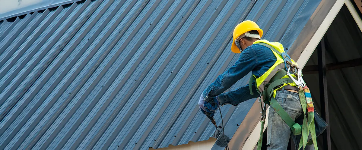 Worker in safety gear installing a metal roof on a commercial building.