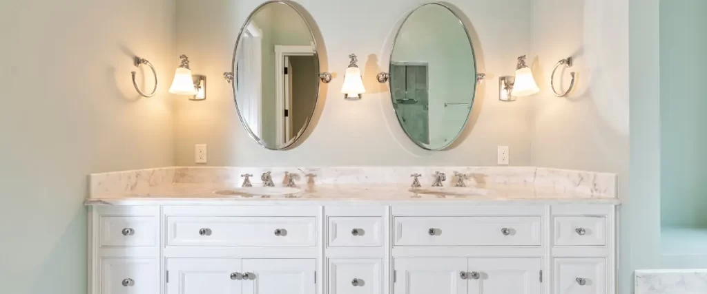 Classic white double vanity with marble countertops and oval mirrors