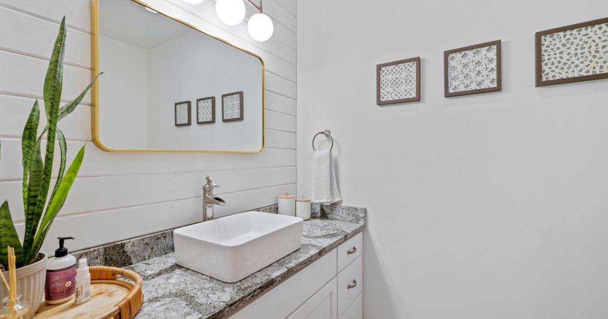 Modern white bathroom vanity with vessel sink, gold-framed mirror, and decorative wall art