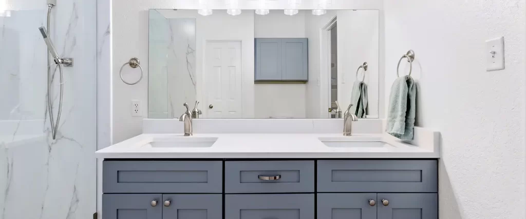 A stylish bathroom remodel featuring a navy blue vanity, quartz countertop, and a glass-enclosed shower.