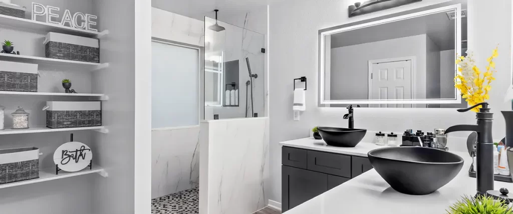 Elegant bathroom with a black vanity, vessel sinks, LED mirror, and a walk-in shower with marble tile.