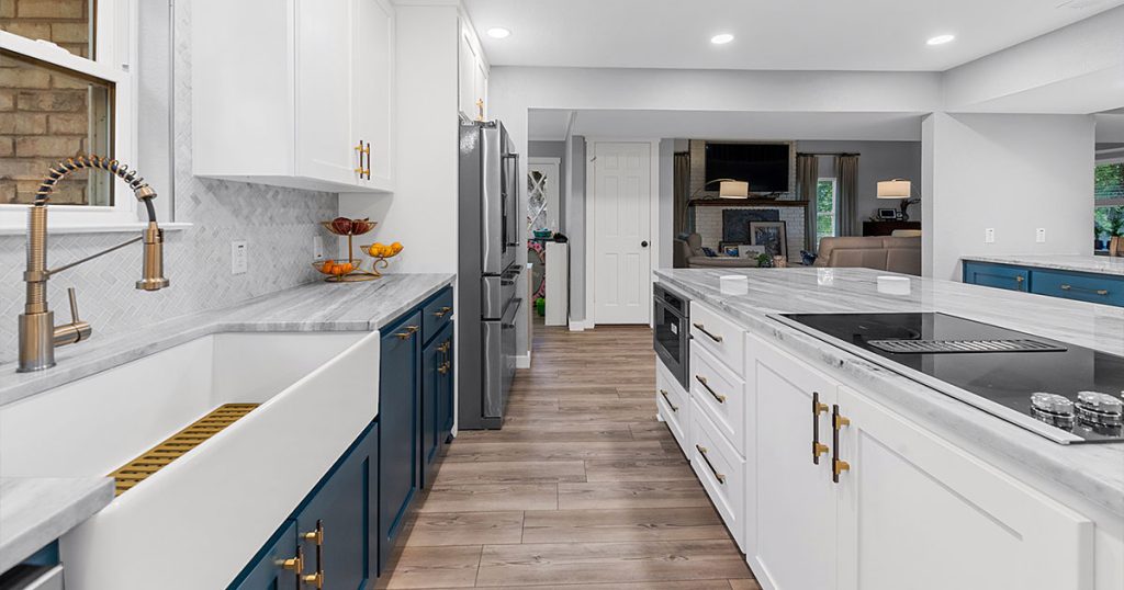 Elegant kitchen with blue lower cabinets, white uppers, marble countertops, and a farmhouse sink. High-end kitchen renovation ideas.