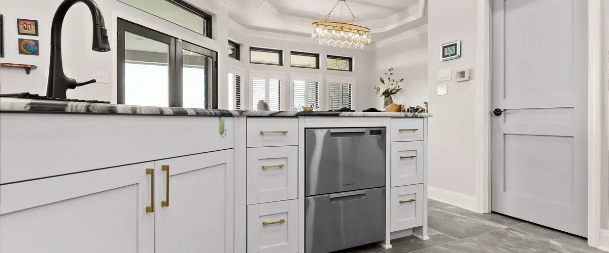 Modern kitchen island with white shaker cabinets, black faucet, stainless steel dishwasher, and marble countertops.