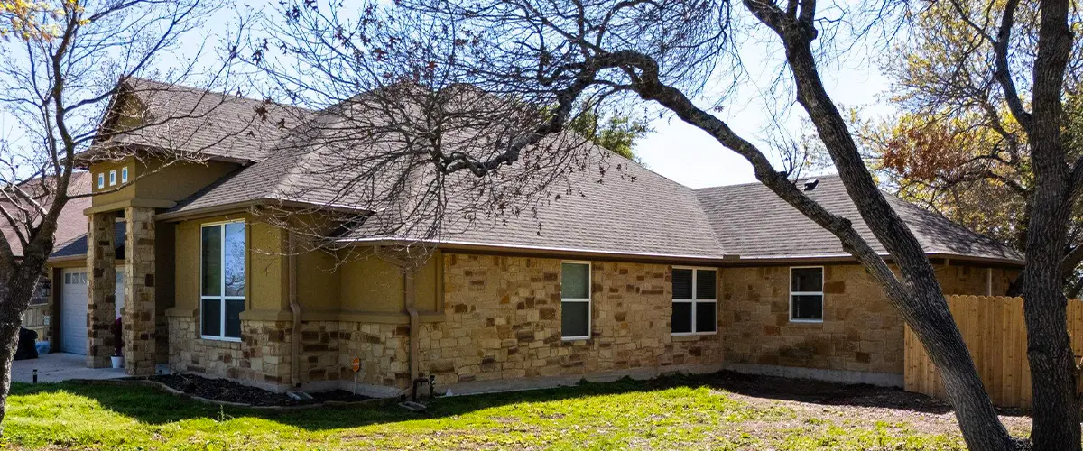 Single-story stone and stucco home with gable roof and attached garage on a partially shaded lot.