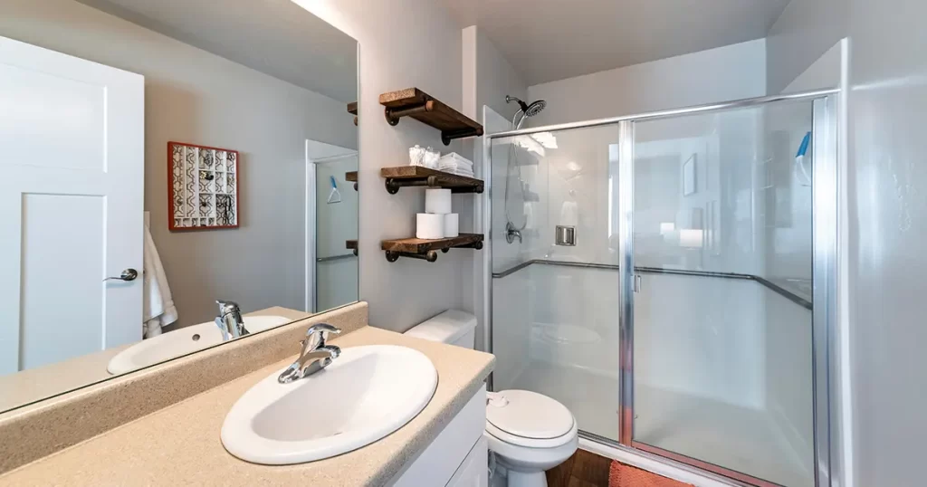 Compact bathroom with sliding glass shower and rustic shelves