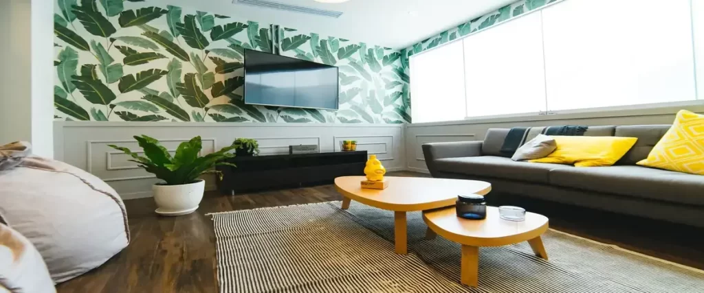 A modern living space featuring bold, tropical leaf wallpaper on the wall behind a mounted television, with a couch and contemporary coffee tables.
