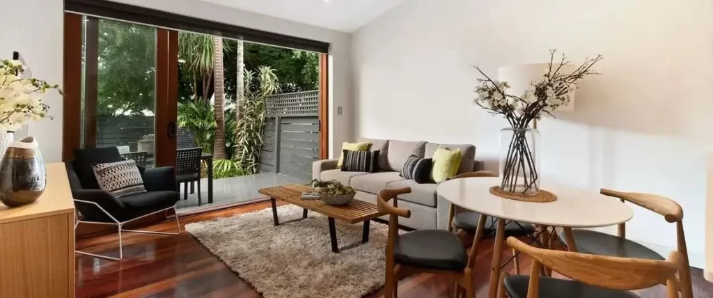 A small, bright living and dining area with dark hardwood floors, connected to an outdoor patio via large glass sliding doors with dark wood frames.