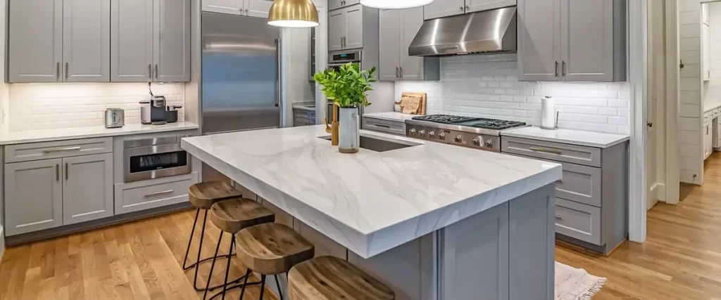 A modern kitchen featuring gray shaker cabinets, a white subway tile backsplash, and a large central island with a waterfall white marble-look quartz countertop.