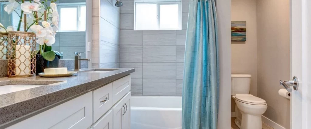 Modern bathroom with white vanity, quartz countertop, and blue shower curtain over bathtub.