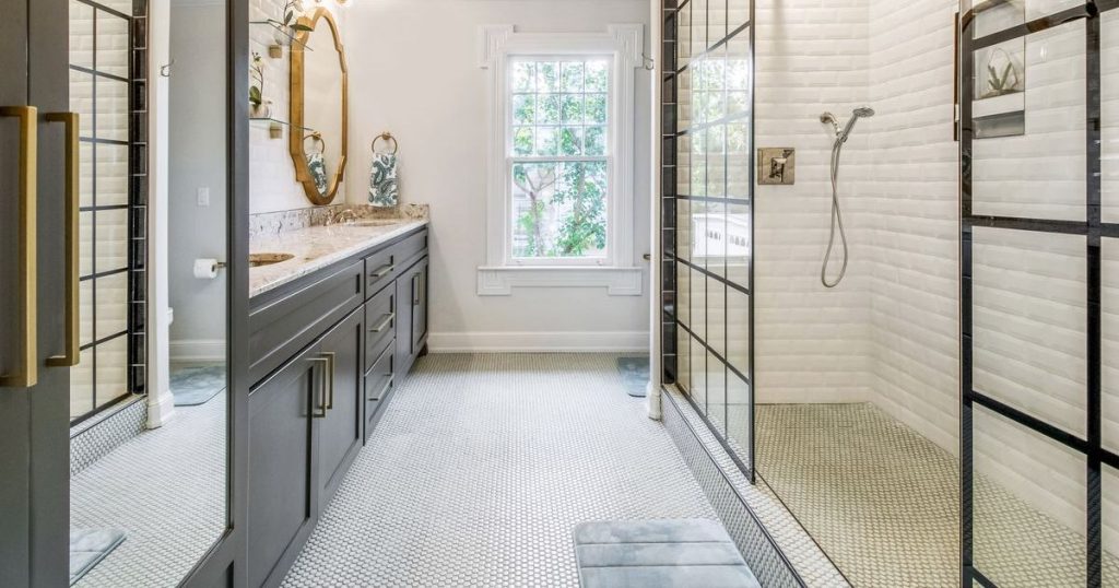 Luxurious modern bathroom featuring a large walk-in shower with grid-patterned glass walls, white subway tile, a gray vanity, and small hexagonal floor tiles.