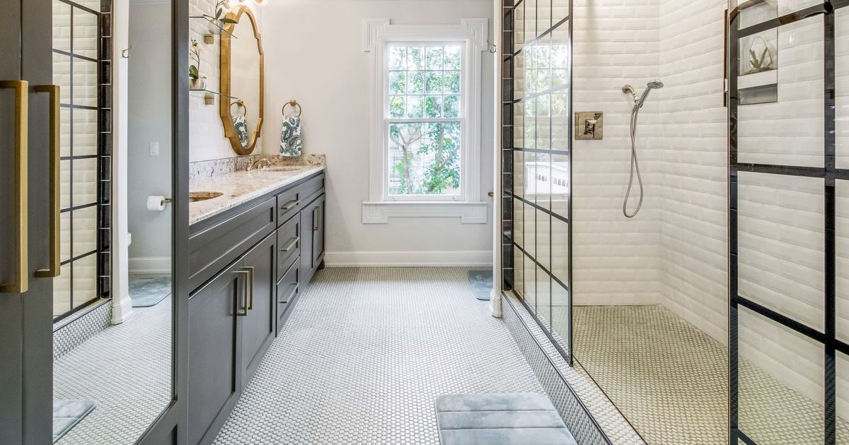 Luxurious modern bathroom featuring a large walk-in shower with grid-patterned glass walls, white subway tile, a gray vanity, and small hexagonal floor tiles.