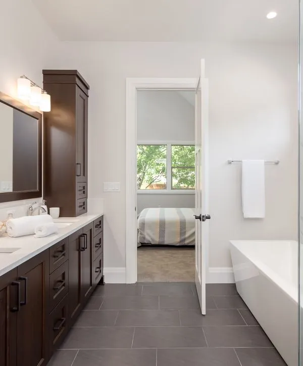 Newly renovated master bathroom featuring a dark wood double vanity, white freestanding tub, and dark gray floor tiles. View into bedroom.