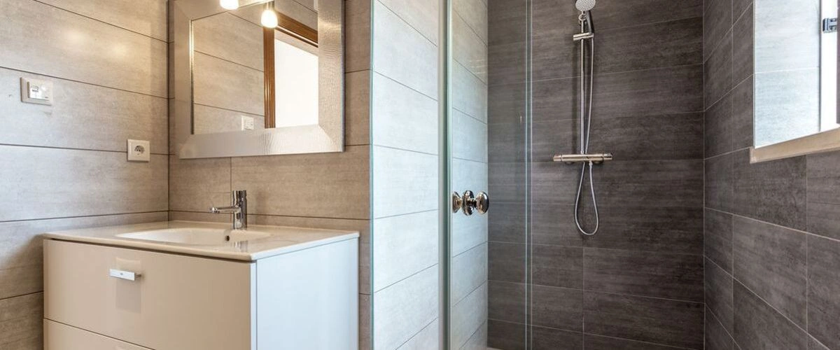 Standard bathroom with a white tub/shower unit, small vanity, mirror, medicine cabinet, and a grey and yellow chevron shower curtain.