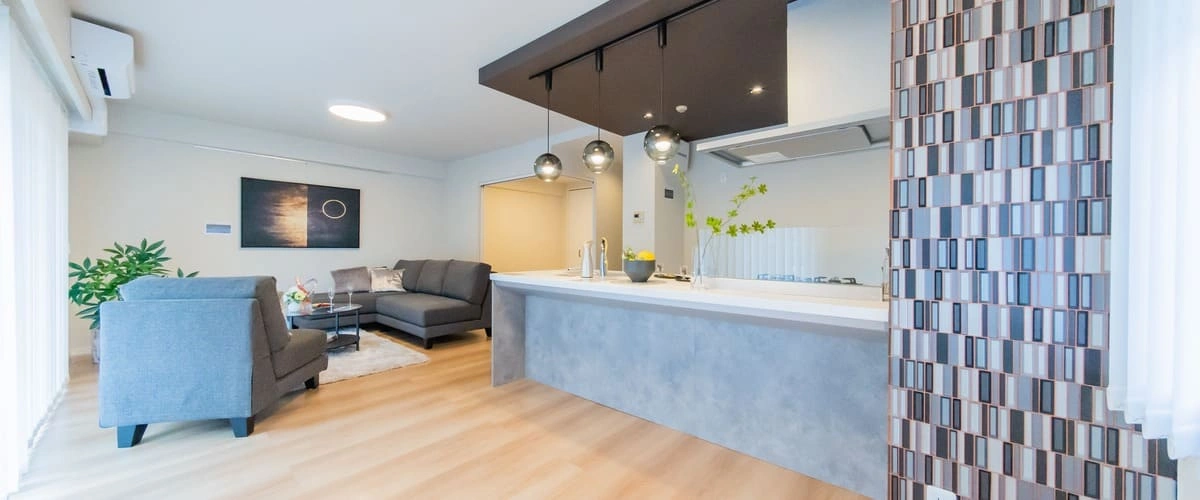 Interior view of a high-end garage conversion showing a modern open-concept living area with grey sofas, a sleek kitchen breakfast bar with pendant lights, and light wood flooring.