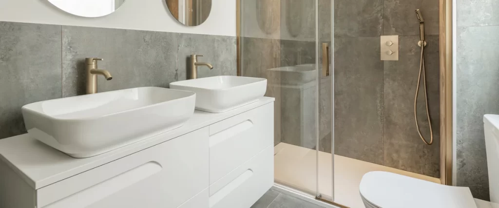 Modern master bathroom design with a double vanity sink and a walk-in shower featuring a seamless frameless glass enclosure and brushed gold hardware.