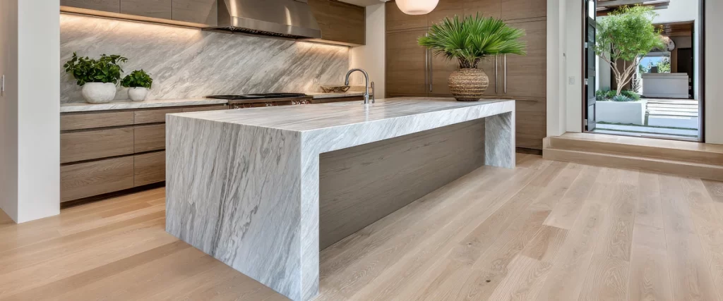 Large marble kitchen island with a waterfall edge design in a modern kitchen with light hardwood flooring.