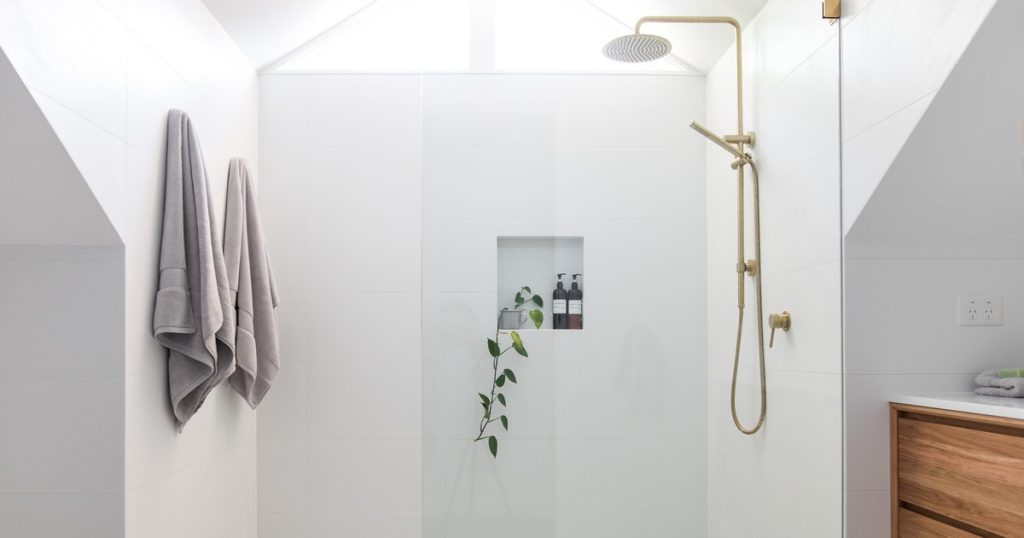 A bright and airy modern white walk-in shower with gold fixtures and a built-in niche, demonstrating how to convert a bathtub to a shower effectively.