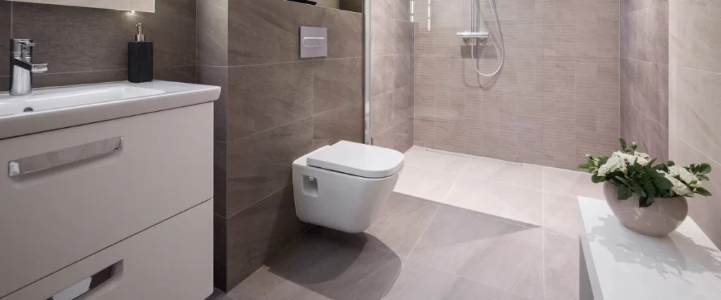 A sleek bathroom interior with floor-to-ceiling grey stone tiles featuring a minimalist wall-hung modern toilet and an open shower area.
