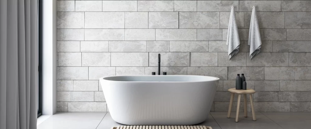 A modern minimalist bathroom featuring a sleek white oval freestanding tub set against a textured grey stone tile accent wall.