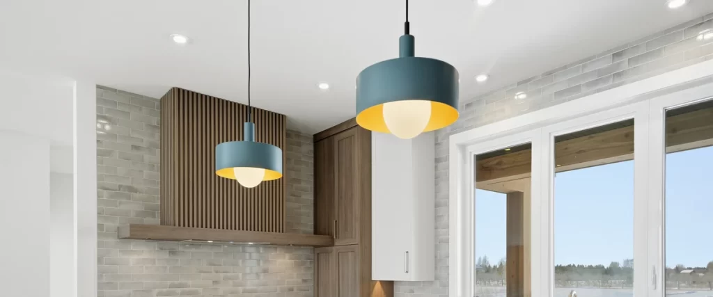 Two industrial-style blue and gold pendant light fixtures hanging over a kitchen counter with tiled backsplash.