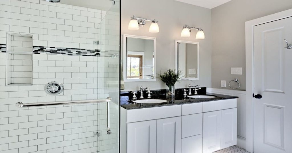 A bright modern bathroom featuring white subway tiles in the shower, a black granite double vanity, and chrome fixtures.