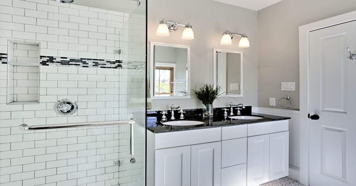 A bright modern bathroom featuring white subway tiles in the shower, a black granite double vanity, and chrome fixtures.