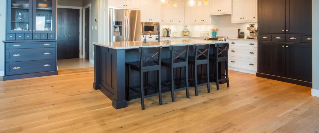 Light-colored oak hardwood floor in a spacious kitchen featuring a dark blue island and breakfast bar seating.