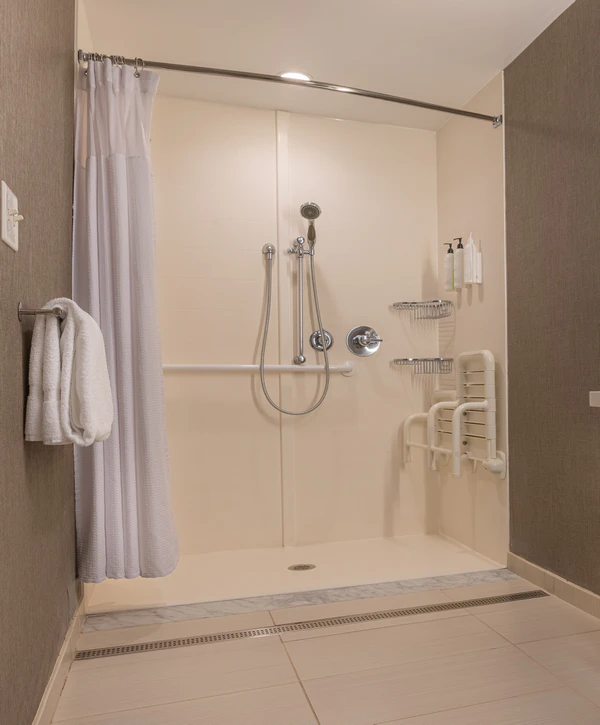An accessible roll-in shower remodeling project in Salado, TX featuring safety grab bars, a fold-down bench seat, and handheld shower spray.