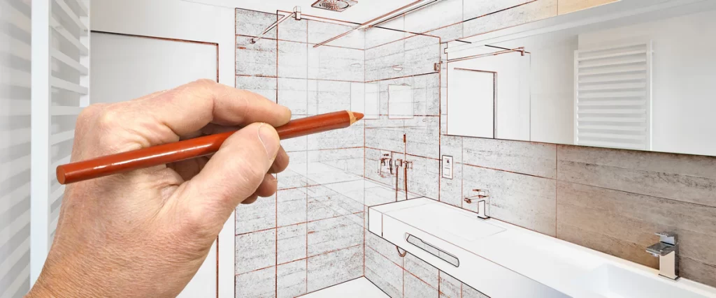 A hand using a red pencil to sketch a new bathroom layout over a photo of a room during the design phase.