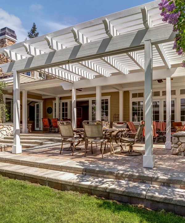 A large, classic white wooden pergola with decorative rafter tails built over a stone patio with an outdoor dining set in Salado, TX.