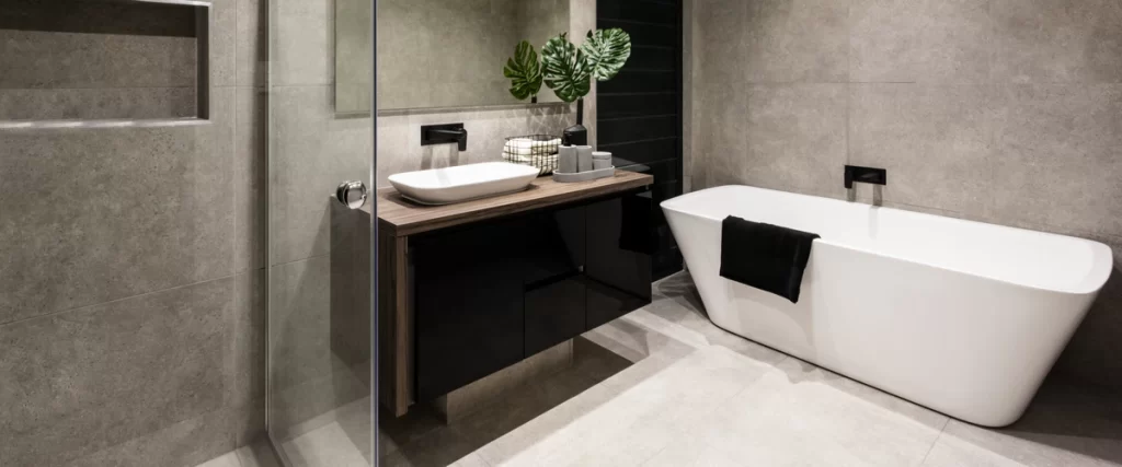 A modern bathroom featuring dark grey textured tile walls, a black vanity with a wood top, a white vessel sink, and a sleek white freestanding bathtub.