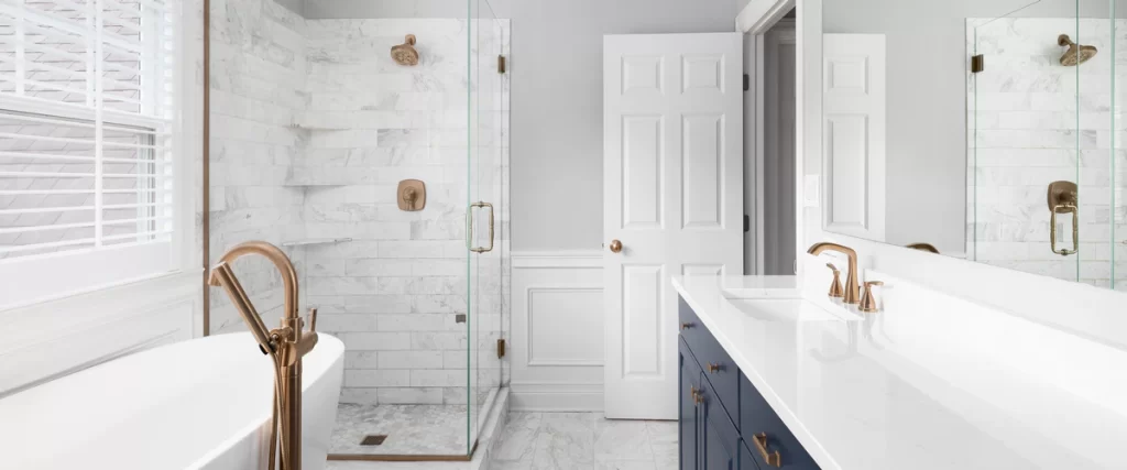 An elegant bathroom design featuring a navy blue vanity with gold faucets and a walk-in shower with white marble subway tiles and gold fixtures.