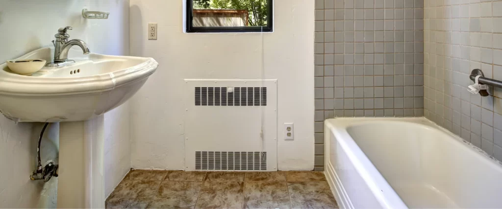 An old bathroom in need of renovation featuring a classic white pedestal sink, dated square wall tiles, and aged flooring.