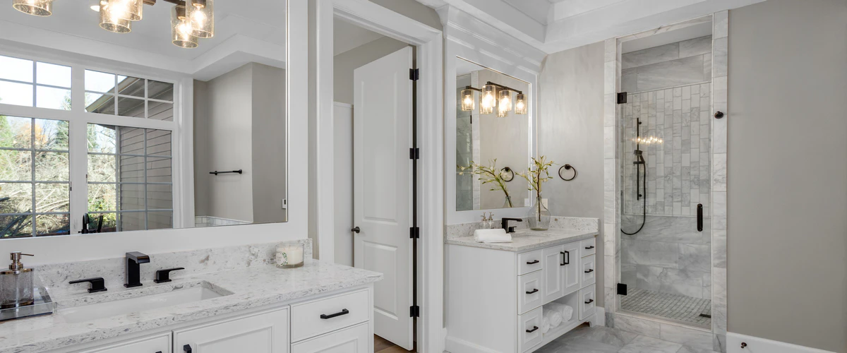 A classic white bathroom design featuring custom white vanities with black hardware and a glass-enclosed shower fitted with light grey subway tiles.