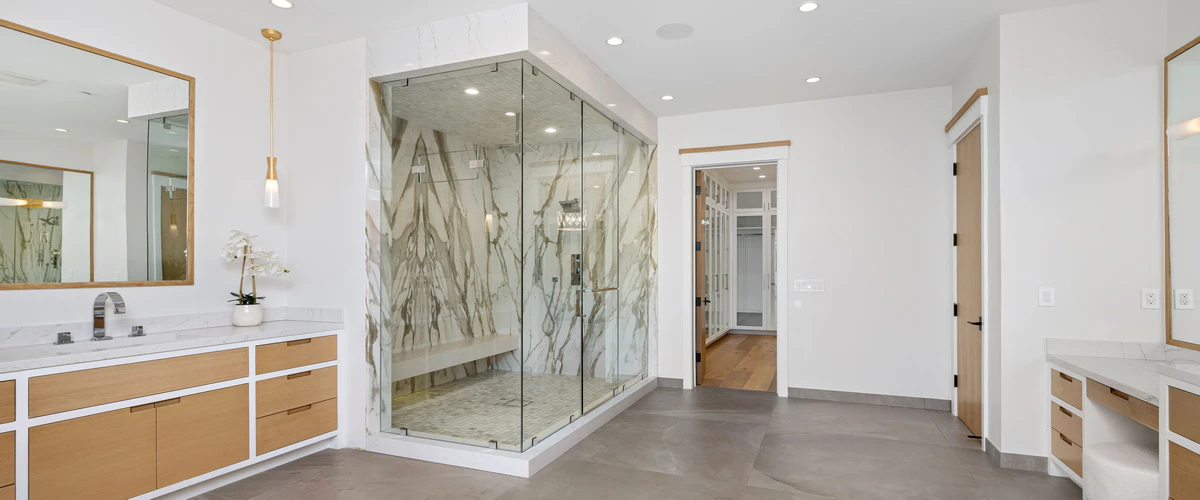 A spacious bathroom showcasing a large walk-in shower with striking marble walls and a built-in bench, paired with an elegant light wood double vanity.