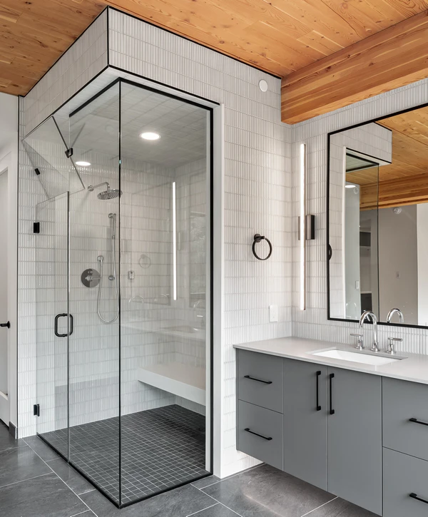 A modern shower remodeling project in Killeen, TX featuring a black-framed glass shower enclosure, white vertical subway tiles, a wood ceiling, and a grey double vanity.