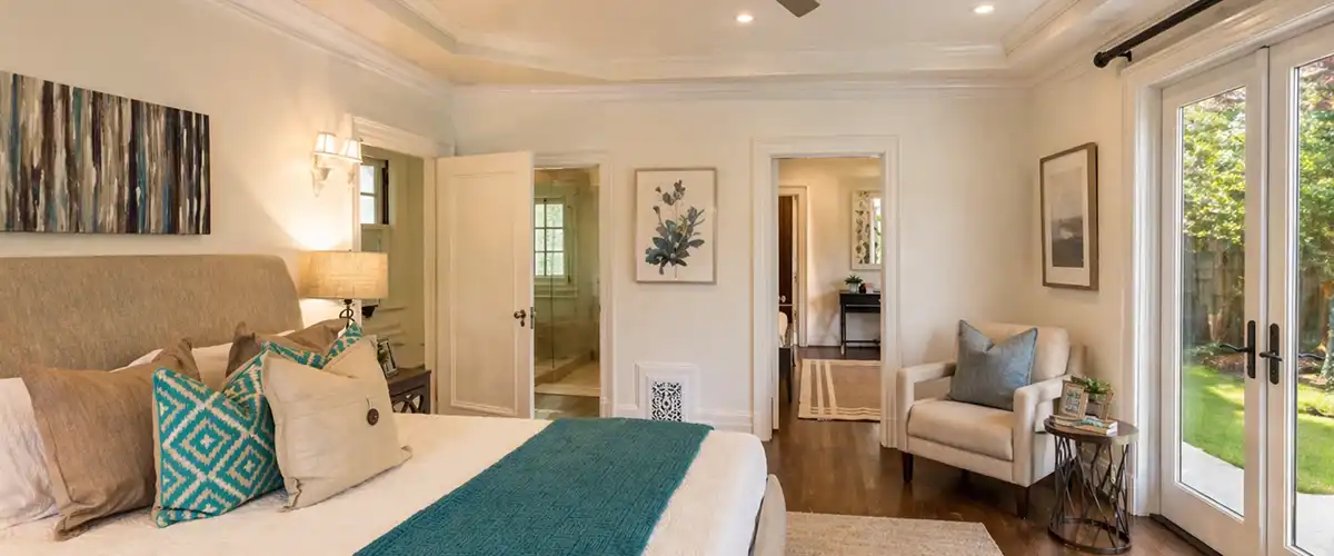 Primary bedroom home addition with tray ceiling, French doors, hardwood floors, and natural light.