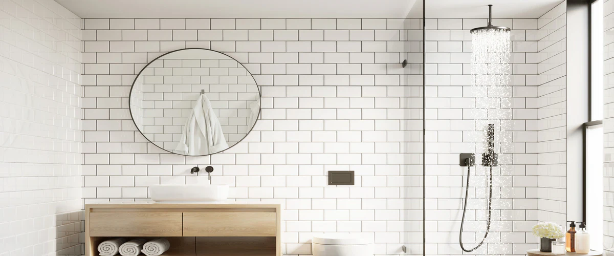 A bright bathroom design with white subway tile walls, a ceiling-mounted black rain shower head, and a large round mirror above a light wood vanity.