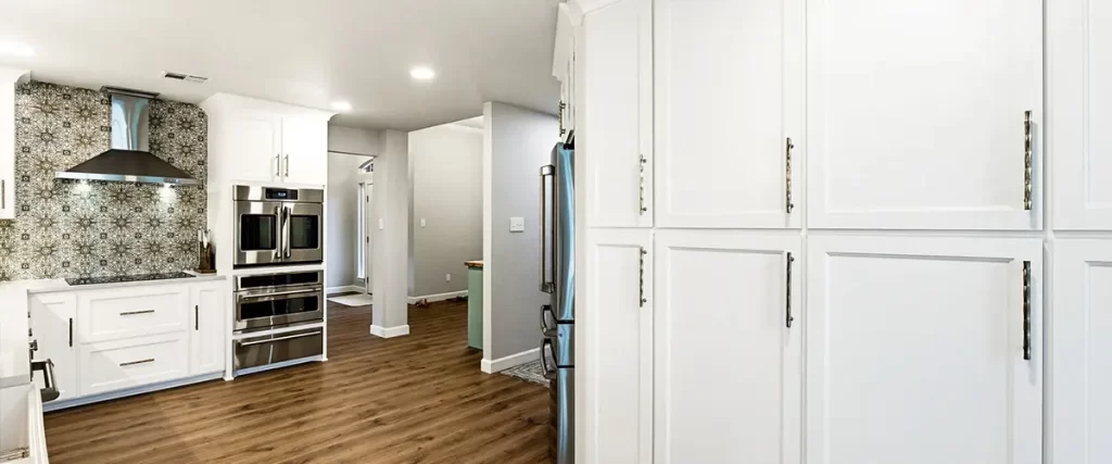 Spacious white kitchen renovation with custom cabinetry, wood flooring, and stainless appliances