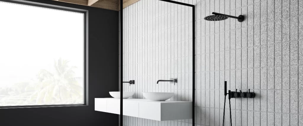 A minimalist bathroom showcasing a white square tiled shower wall with matte black fixtures, alongside a modern white floating double sink vanity.