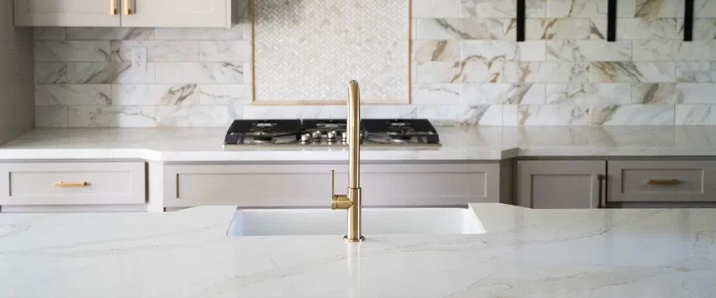 Luxury kitchen remodel with quartz countertops, marble backsplash, and brass faucet over island sink