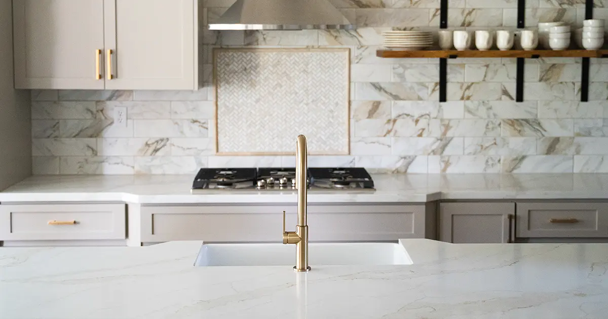 Luxury kitchen remodel with quartz countertops, marble backsplash, and brass faucet over island sink