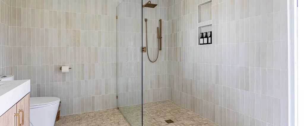 Luxury walk-in shower renovation with floor-to-ceiling tile, glass panel, and built-in niche